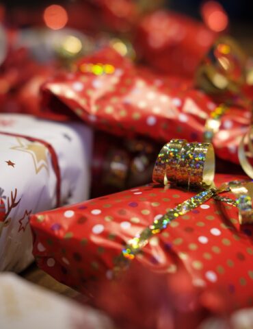 Auf folgenden Bild sind mehrere Rote eingepackte Geschenke zusehen, außerdem haben diese jeweils eine Goldene Glitzende Schleife. Das Bild dient als Hintergrund des Blog beitrages